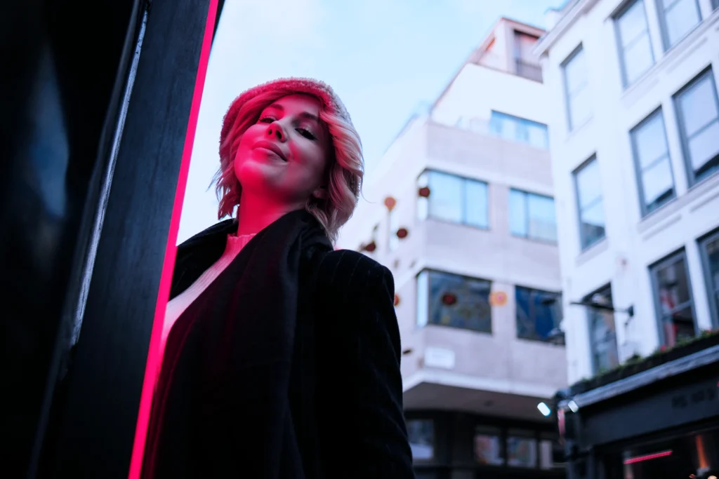 Professional woman in a black blazer lit by a pink neon light against an urban city backdrop