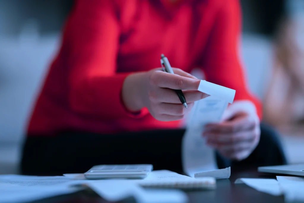 A person in a red top reviewing receipts and paperwork at a desk, representing the admin burden of unmanaged business travel expenses and the value of structured payment terms through a TMC.