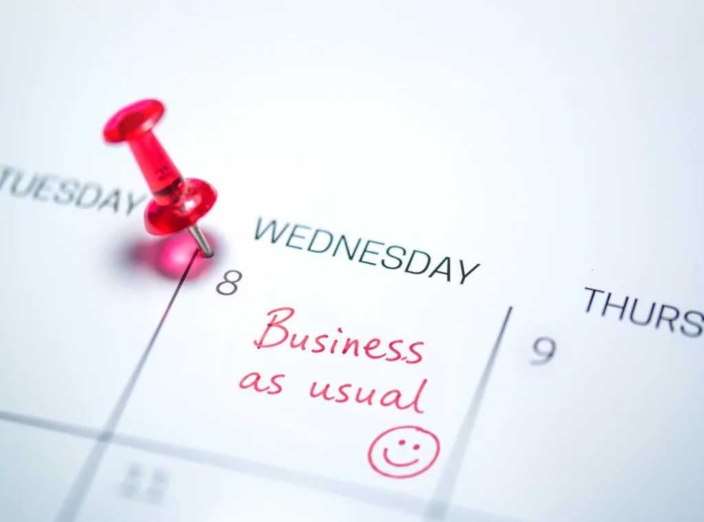 Calendar planner with 'Business as usual' handwritten in red on Wednesday and pinned with a red thumbtack, reflecting the routine nature of cross-border business travel on the island of Ireland
